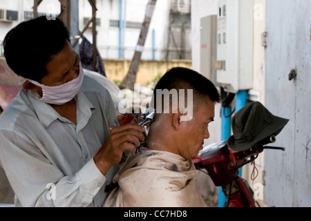 Ein Friseur gibt einem Mann einen Haarschnitt in einem Barbershop auf einer Stadtstraße in Phnom Penh, Kambodscha. Stockfoto