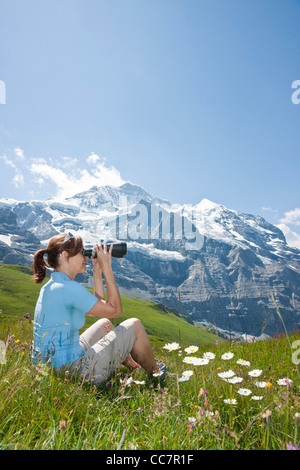 Frau sitzt auf der Bergseite mit Fernglas, Berner Oberland, Schweiz Stockfoto