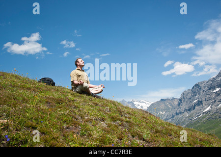 Mann sitzt auf der Bergseite, meditieren, Berner Oberland, Schweiz Stockfoto