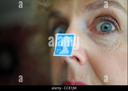 Applying Frau nahe Gesicht mit einem britischen zweiten 2. Klasse Briefmarke klebte an Nase Modell Stockfoto