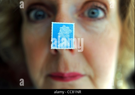 Applying Frau nahe Gesicht mit einem britischen zweiten 2. Klasse Briefmarke klebte an Nase Modell Stockfoto