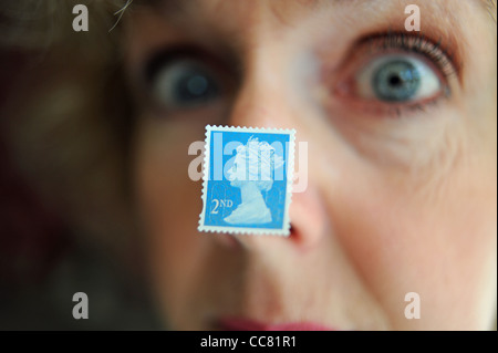 Applying Frau nahe Gesicht mit einem britischen zweiten 2. Klasse Briefmarke klebte an Nase Modell Stockfoto