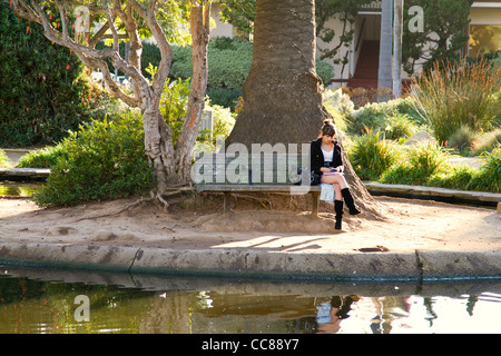 Junge Frau auf der Bank neben Teich in Alice Keck Park in "Santa Barbara", California Stockfoto