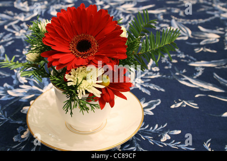 rote und weiße Blüten in eine Tasse als Herzstück auf einem blau floral Tischdecke Stockfoto