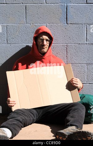 Obdachloser in rotes Sweatshirt mit einem leeren Karton Schild Stockfoto