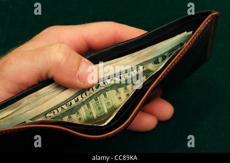 die Hand eines Mannes hält eine Leder-Portemonnaie mit US-Rechnungen offen auf einem grünen Hintergrund gefüllt Stockfoto