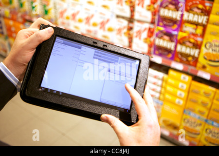 Handheld Tablet in einem Supermarkt Regal für die Übernahme von Getreide durch die Mann in Anzug, Armen hielt nur Stockfoto