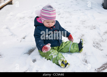 Babymädchen Schnee Anzug sitzen am Boden im Schnee Stockfoto