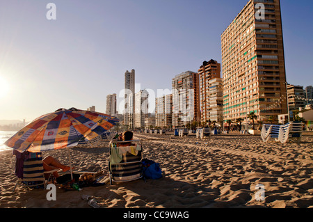 Touristen sitzen am Strand von Playa Levante, Benidorm, Costa Blanca, Spanien Stockfoto