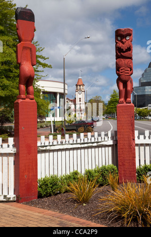 Rotorua, Neuseeland. Maori Totems am Eingang zum Stadtpark. Stadt Uhrturm in Ferne. Stockfoto