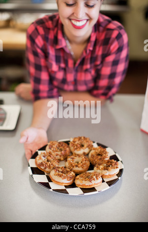 Junge Frau, die Halteplatte an frisch gebackenen Kuchen in der Bäckerei Stockfoto