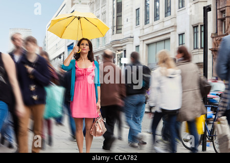 Mitte Erwachsene Frau im rosa Kleid stehen noch mit Regenschirm in überfüllten Stadt Stockfoto
