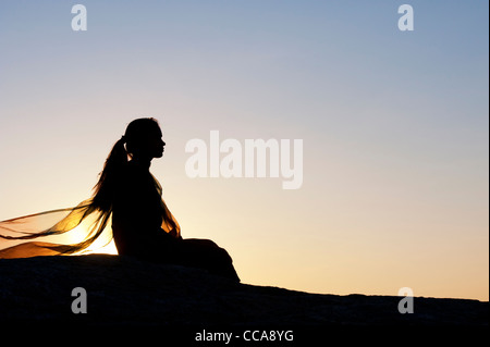Indisches Mädchen ganz allein auf einem Stein saß bei Sonnenuntergang. Silhouette. Andhra Pradesh, Indien Stockfoto