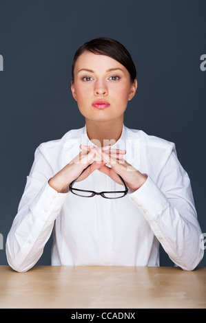 Schöne europäische junge solide Geschäftsfrau mit Brille vor grauem Hintergrund sitzen Stockfoto