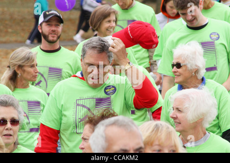 Mann mit rotem Hut, umgeben von einer Menge von grünen Hemden. Alzheimer Speicher zu Fuß. Stockfoto