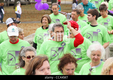 Mann mit rotem Hut, umgeben von einer Menge von grünen Hemden. Alzheimer Speicher zu Fuß. Stockfoto