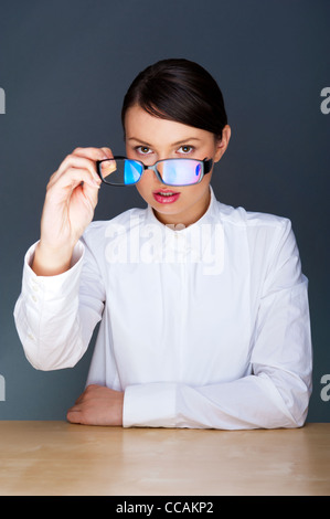 Schöne europäische junge solide Geschäftsfrau mit Brille vor grauem Hintergrund sitzen Stockfoto