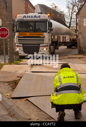 Außergewöhnlicher Konvoi für den Transport einer Windkraftanlage. Blechplatten auf dem Boden ermöglichen das Schneiden der Biegung. Ein Pilot führt den Fahrer. Stockfoto