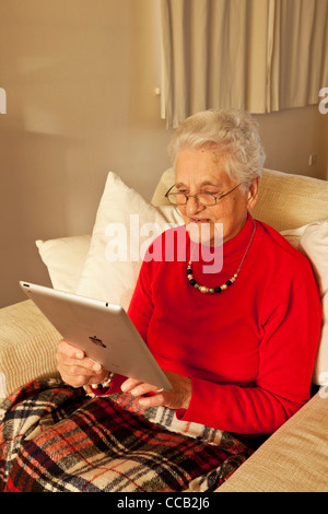 Alte Frau mit einem Ipad 2-Tablet Computer saß in einem Sessel mit Brille im Inneren Stockfoto