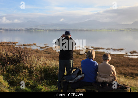 Drei Menschen betrachten die über Traeth Abermenai und die Menai Strait von Newborough Warren Anglesey Wales UK Stockfoto