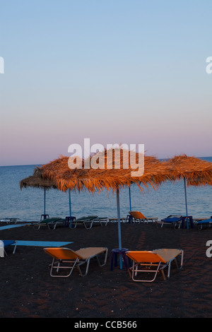 Sonnenschirme und liegen bei Sonnenuntergang in Perissa Beach, Santorin, Griechenland Stockfoto