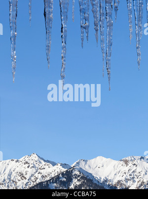 Großen Eiszapfen vor blauem Himmel mit schneebedeckten Bergen im Hintergrund Stockfoto