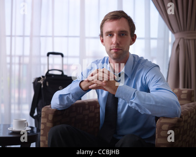 Porträt von glücklich kaukasischen Geschäftsmann mit gekreuzten Fingern lächelnd in die Kamera im Hotelzimmer während der Geschäftsreise. Vorderansicht Stockfoto