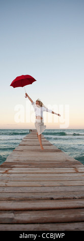 Junge Frau am Pier halten Dach springen Stockfoto