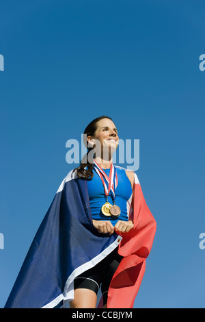 Sportlerin auf Siegertreppchen, eingehüllt in französische Flagge Stockfoto