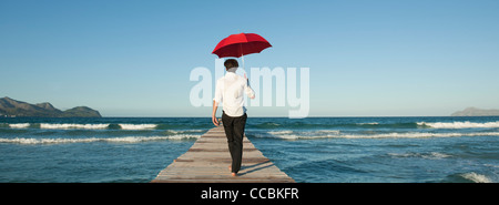 Mann zu Fuß auf Pier mit Regenschirm, Rückansicht Stockfoto