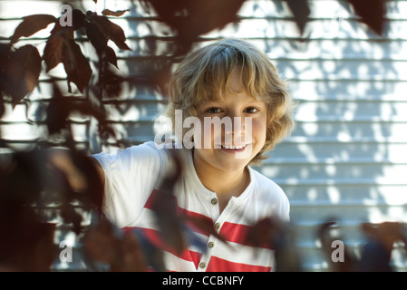 Junge lächelnd hinter Ästen Stockfoto