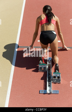 Frau kauerte in Startposition auf Laufstrecke, Rückansicht Stockfoto
