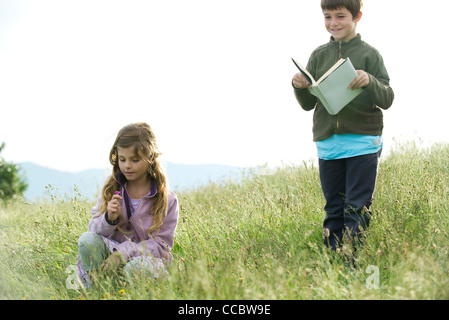 Im Bereich Kinder, nimmt Junge liest Buch während Girl Wildblumen Stockfoto