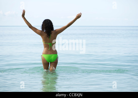 Frau im Bikini stehen im Ozean mit Armen, Rückansicht Stockfoto