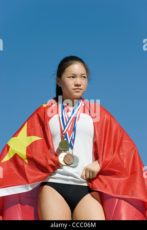 Sportlerin auf Siegertreppchen, eingehüllt in chinesische Flagge Stockfoto