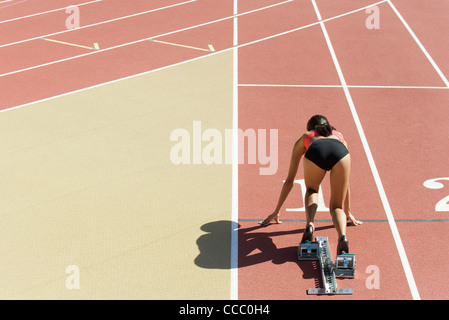 Frau kauerte in Startposition auf Laufstrecke, Rückansicht Stockfoto