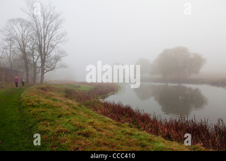 Zwei Läufer gehen am kleinen Teich in Home Park, Hampton Court in der Nähe von Hampton Wick Tor. Stockfoto