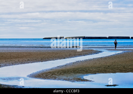 Arromanche, Normandie, Frankreich. Ein Mann geht auf die Seashort. Reste der "Mulberry" künstliche Hafen aus dem zweiten Weltkrieg in den Rücken. Stockfoto