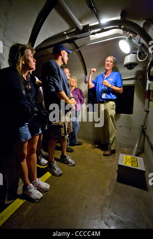 Ein uniformierter Führer erklärt einer Reisegruppe in einem Tunnel Inspektion am Hoover-Damm einen Erdbeben-Detektor (unten rechts). Stockfoto