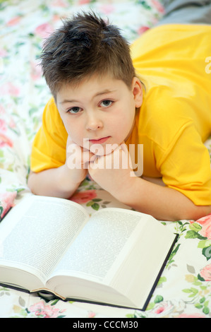 junge Kind 8 9 7 Jahre liest lesen lernen Bildung Buch drucken Lügen Lügen Bett Schlafzimmer Decke Farbe Blumen blühen Caucasi Stockfoto
