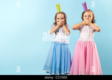 Porträt von Zwillingsmädchen in schönen Kleidern und Kronen zeigt ihr Erstaunen Stockfoto