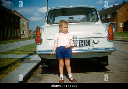 Ein kleiner Junge posiert stolz an der Rückseite des Familienautos Anglia auf einem Landgut von Essex in den frühen sechziger Jahren. Stockfoto