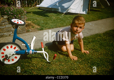 Ein kleiner Junge sitzt im Gras nach einem Sturz von seinem Dreirad an einem Sommertag im Garten der Familie in den frühen sechziger Jahren Stockfoto