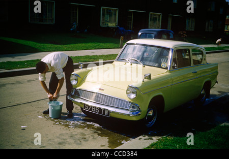 Ein junger Mann wäscht das Familienauto Anglia auf einem Landgut von Essex in den frühen sechziger Jahren. Stockfoto