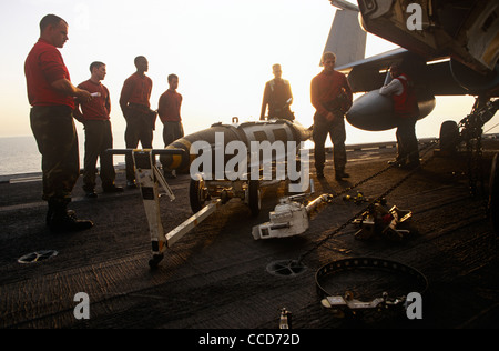 Rote Hemden Ordnance Männer bereiten und intelligente Bomben zu einer F/A-18 Kampfjet auf dem Deck der USS Harry S Truman passen. Stockfoto