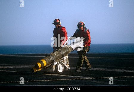 Rote Hemden Ordnance Männer bereiten, intelligente Bomben zu einer F/A-18 Kampfjet auf dem Deck der USS Harry S Truman passen. Stockfoto