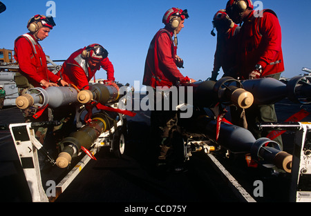 Rote Hemden Ordnance Männer bereiten Sie intelligente Bomben und Raketen, die eine F/A-18 Kampfjet auf dem Deck der USS Harry S Truman passen. Stockfoto