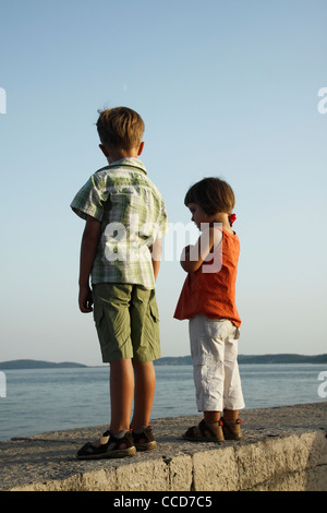 Junge und ein Mädchen mit Blick auf das Meer beim stehen auf einer Steinmauer um Hafen in Orebic, Kroatien Stockfoto