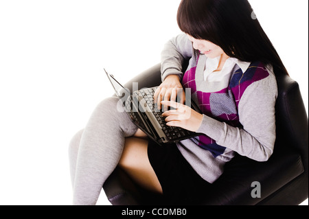 Chinesische Schulmädchen in einem Ledersessel auf einem Laptop arbeiten. Stockfoto