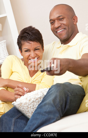 Ein glückliches afroamerikanische Mann und Frau-Paar in den Dreißigern zu Hause sitzen, Essen Popcorn mit Fernbedienung Stockfoto